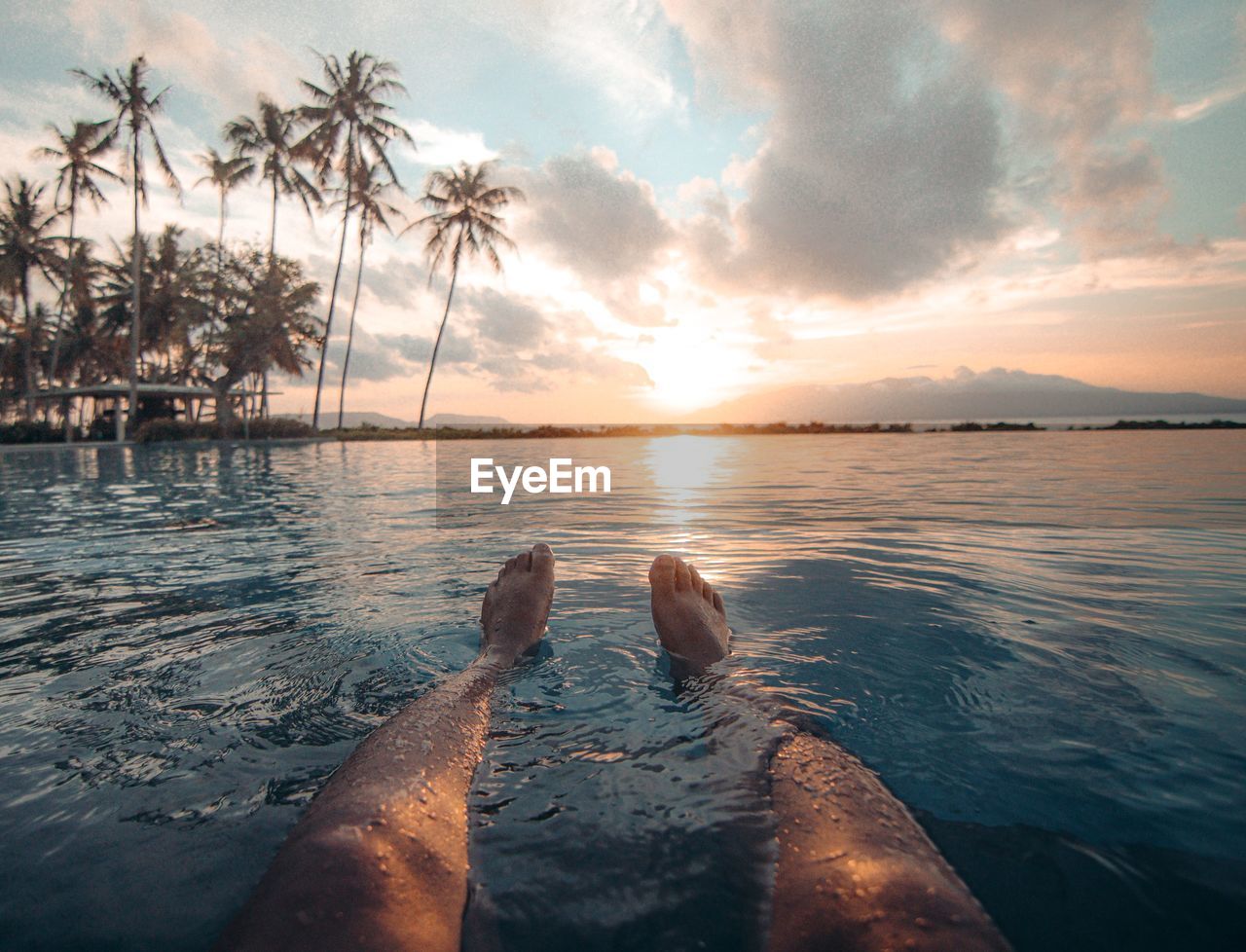 Scenic view with foot floating on sweming pool of sea against sky at sunset