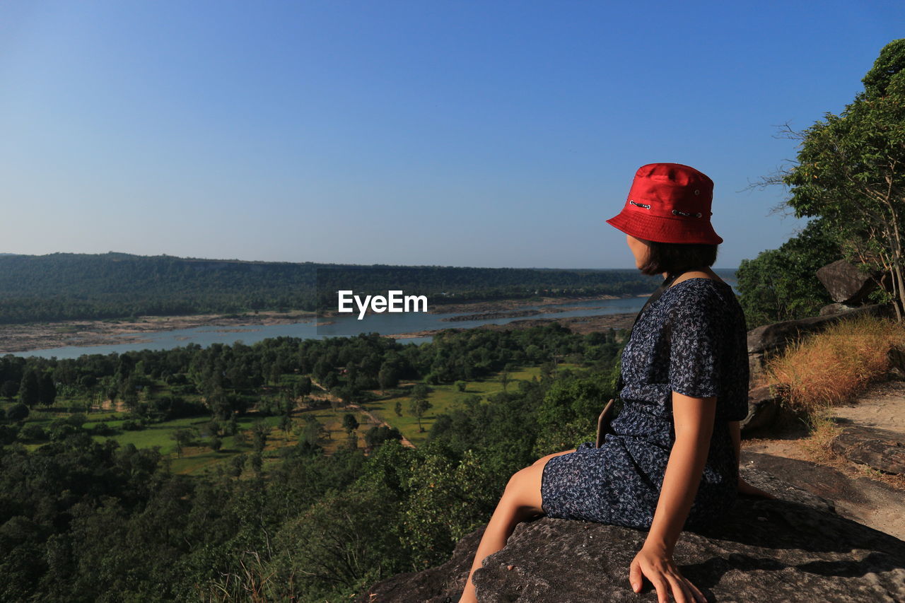 Woman traveler sits and looks at the edge of the cliff.