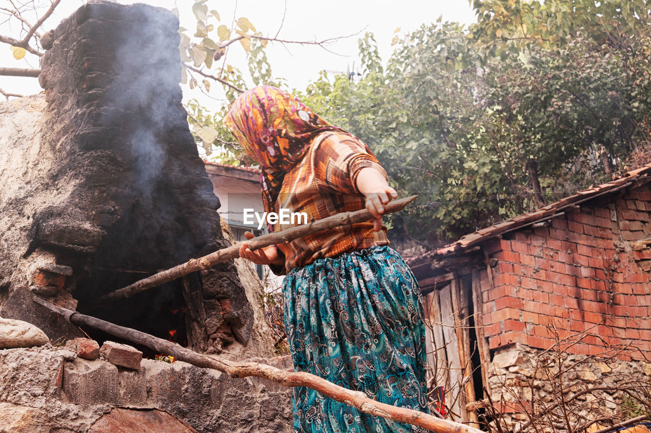 Low angle view of woman putting wood in oven