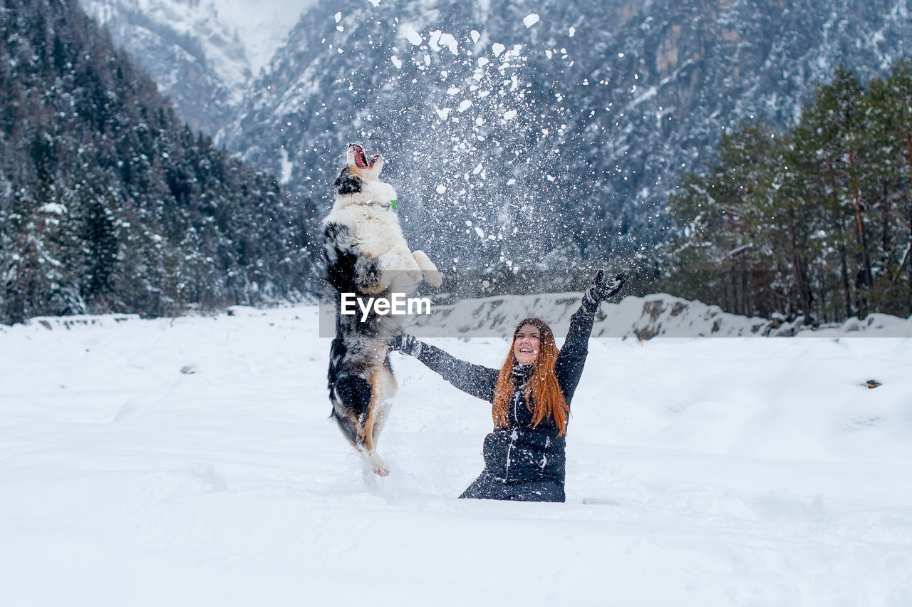 Cheerful woman playing with dog on snow covered field