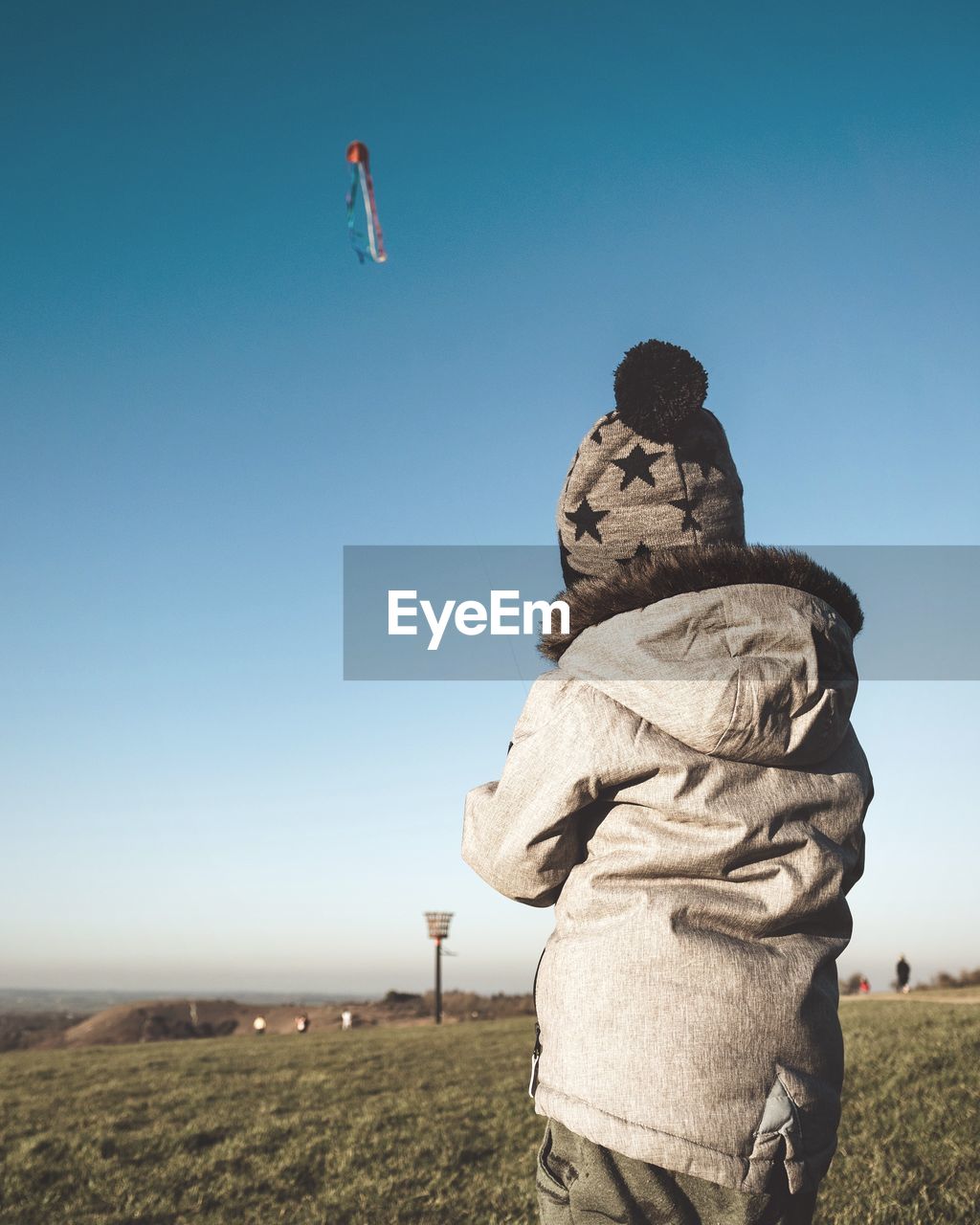 Rear view of boy wearing warm clothing while flying kite against clear sky