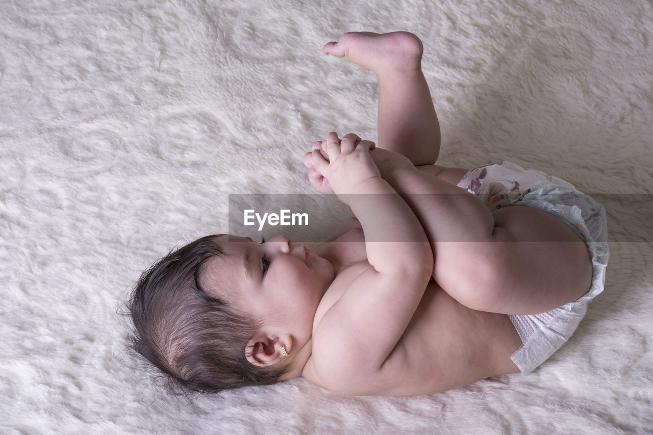 Directly above shot of shirtless baby girl lying on bed