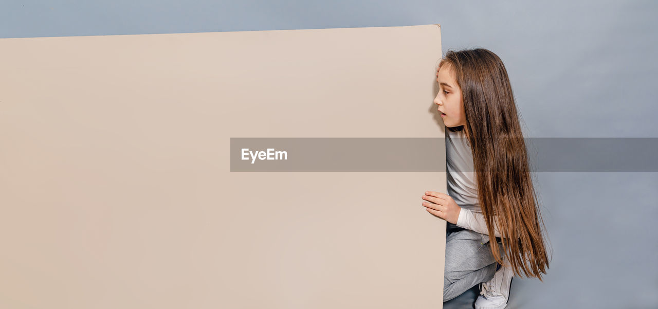 Large sheet of white cardboard. little girl looks surprised at blank banner. advertising.