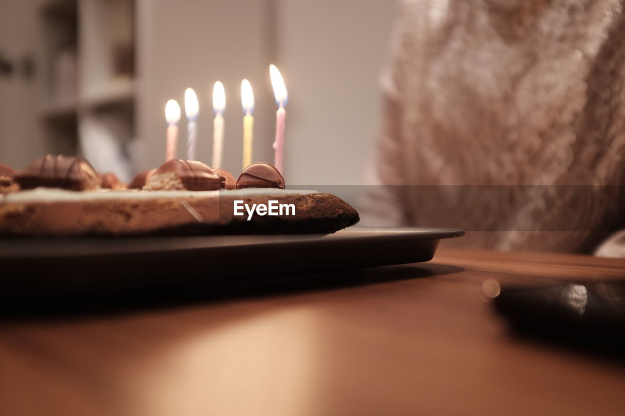 Midsection of person by birthday cake on table