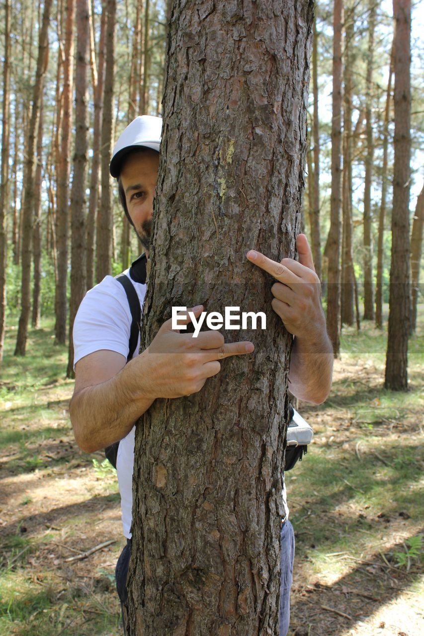 Man doing obscene gesture while embracing tree at forest