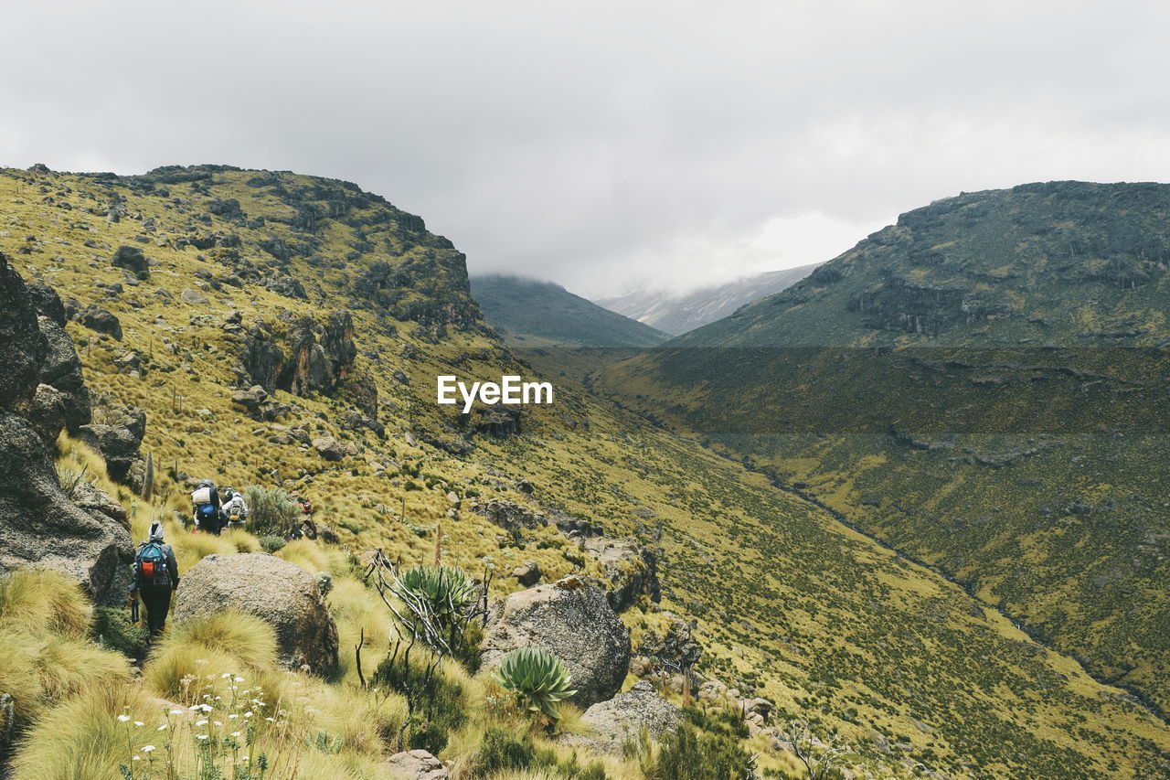 Rear view of hiker walking on mountain against cloudy sky