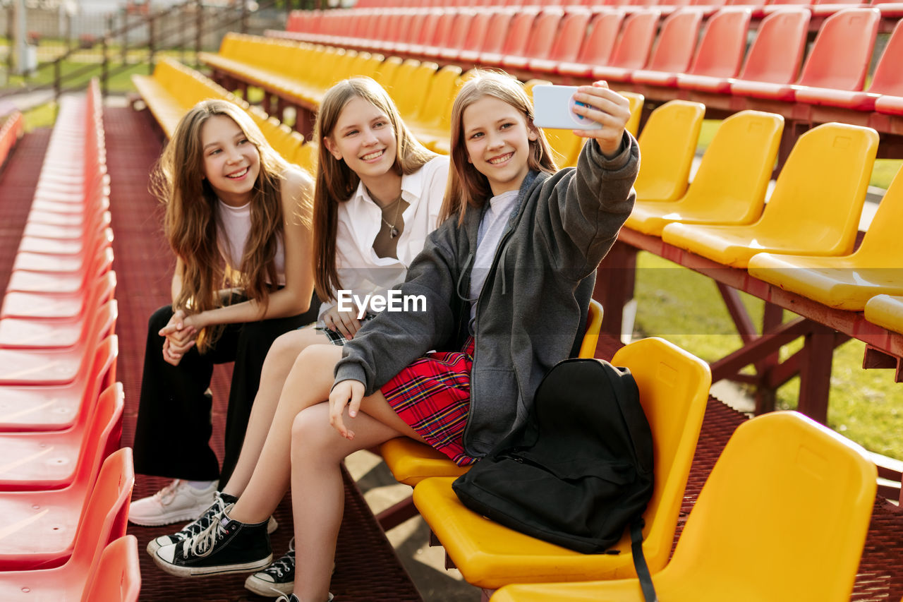 Three charming friends take selfies on their phone at the school stadium. the concept of friendship. 