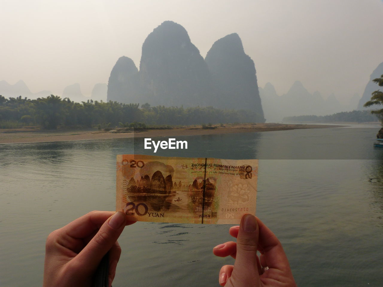 Close-up of hands holding paper currency by river against mountains