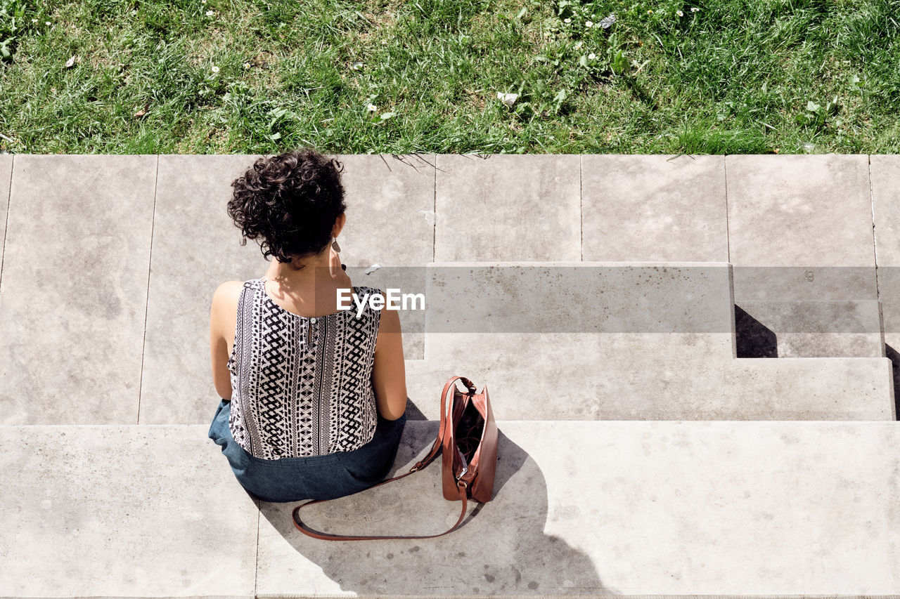 HIGH ANGLE VIEW OF WOMAN SITTING ON COBBLESTONE