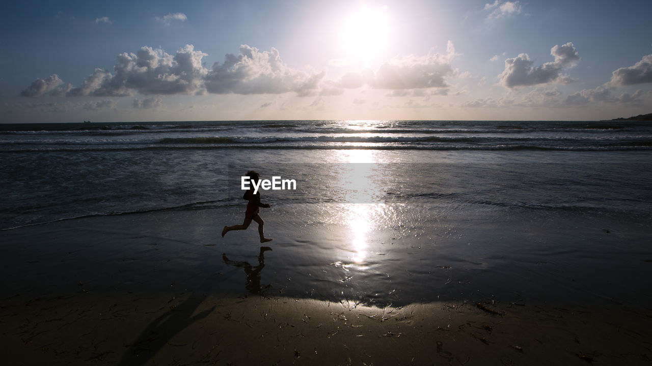 Side view silhouette of boy running on beach against sky