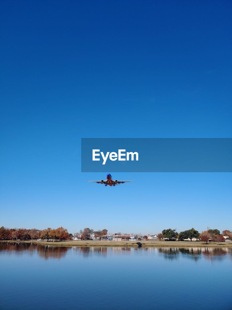 AIRPLANE FLYING OVER LAKE AGAINST SKY