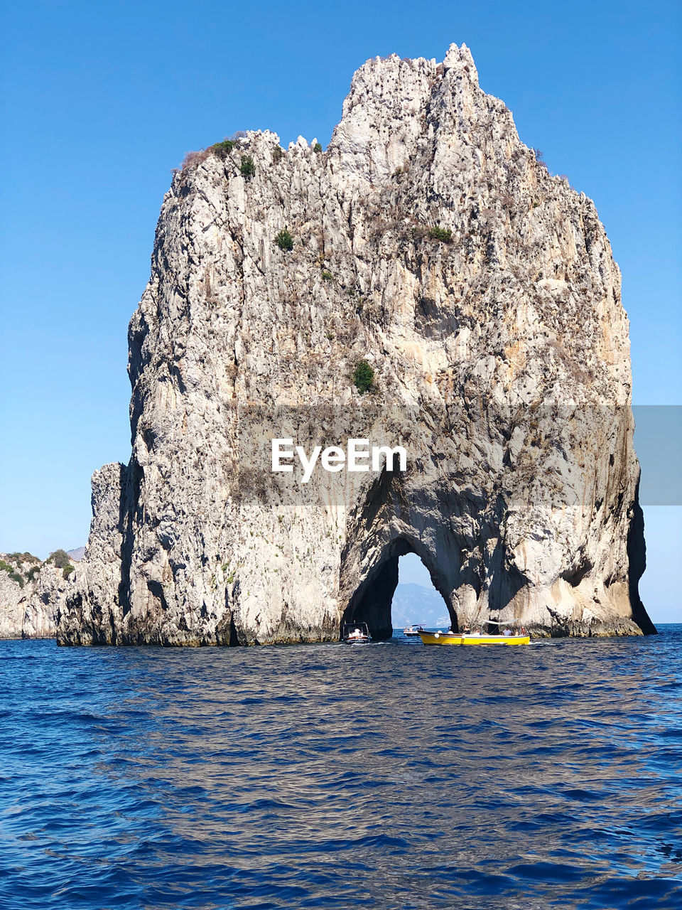 Rock formation by sea against clear blue sky