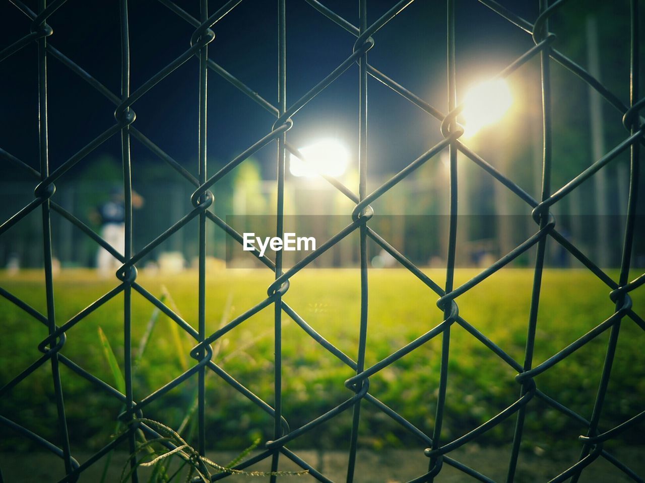 Illuminated baseball diamond seen through chainlink fence