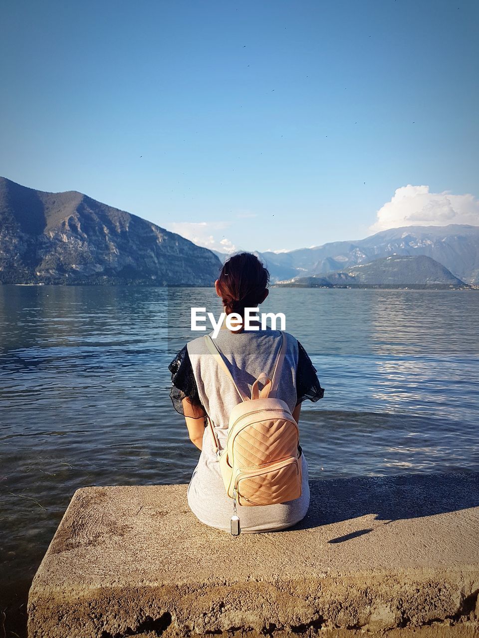 Rear view of woman sitting by lake against mountain