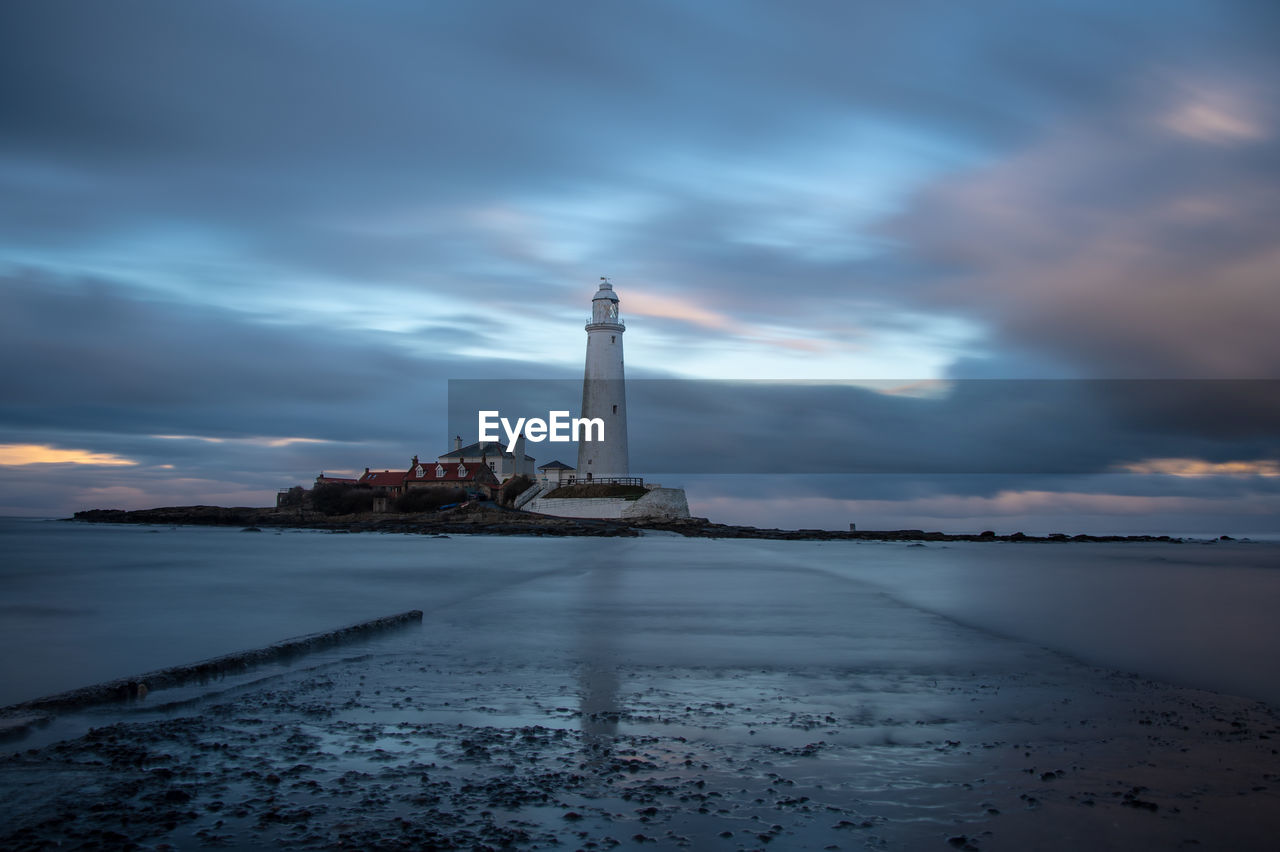 Lighthouse by sea against sky at dusk