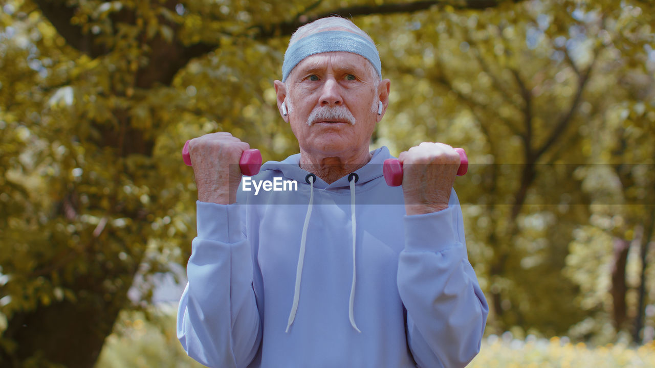 Determined senior man exercising with dumbbells in park