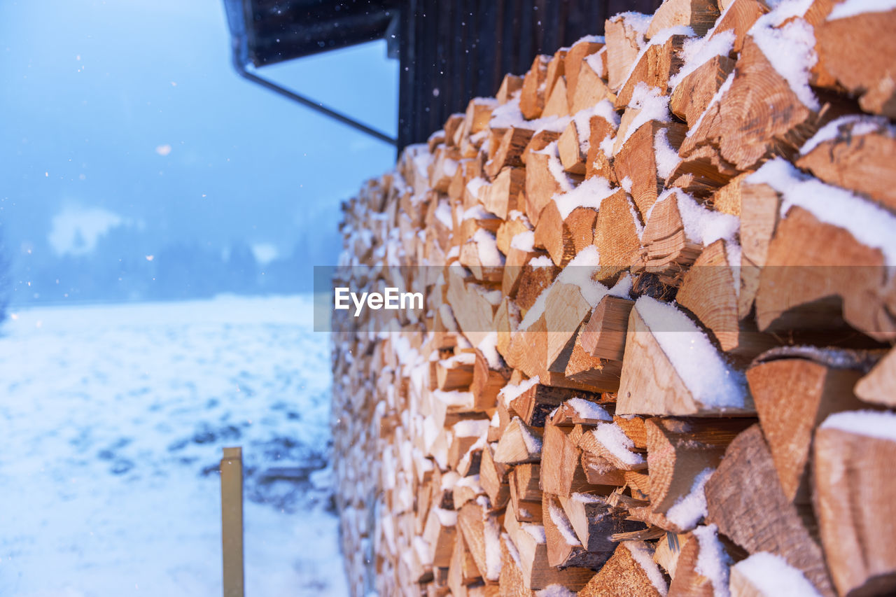 Full-sized side view of freshly beaten, stacked on a barn and snow-covered firewood in snowfall.