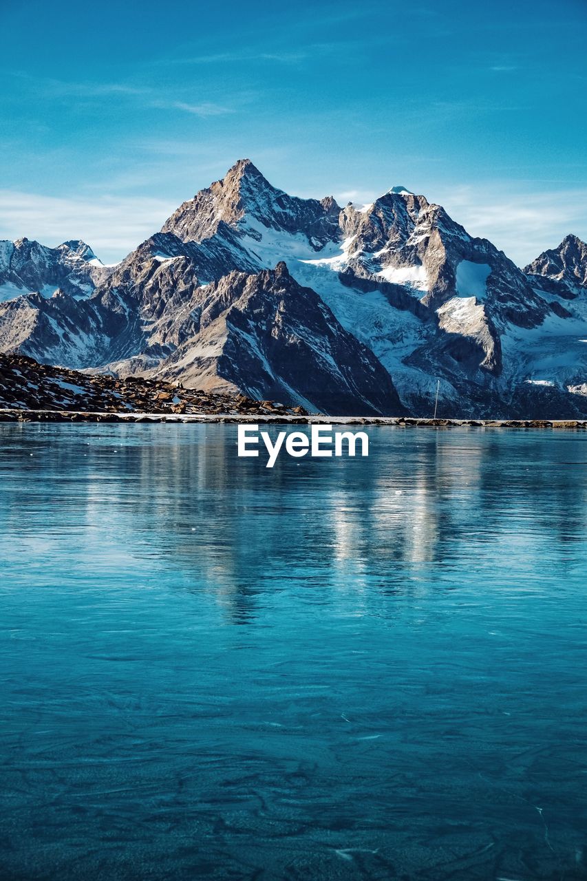 Scenic view of lake and snowcapped mountains against blue sky