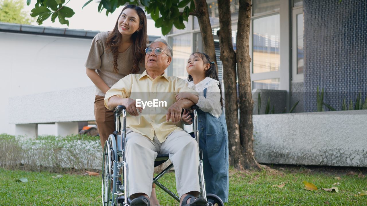 Disabled senior grandpa on wheelchair with grandchild and mother in park