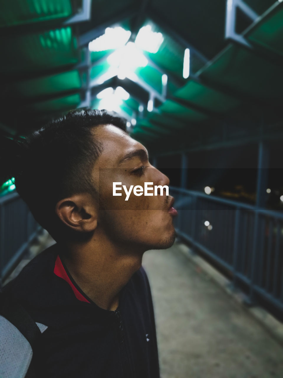 Close-up profile view of young man emitting smoke while standing on elevated walkway