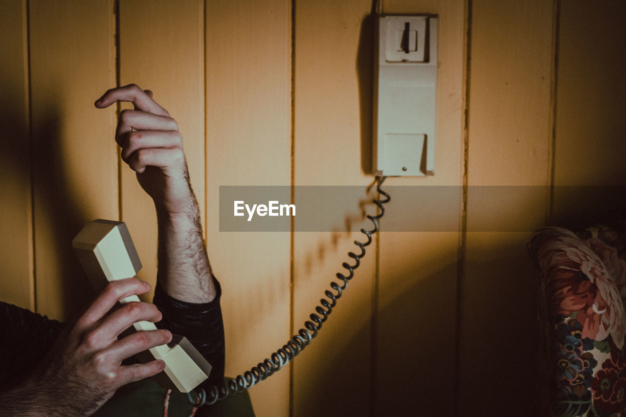 Cropped image of person holding telephone on wall