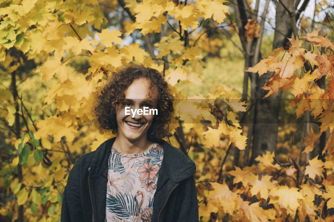 Cheerful teenage boy with braces and curly hair looking away during autumn