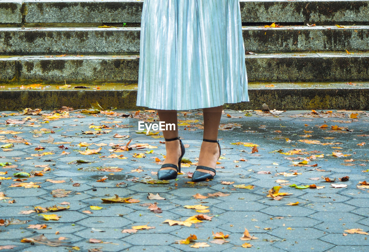 Low section of woman standing by autumn leaves on footpath