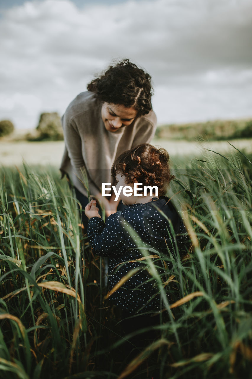 Mother with daughter standing amidst plants against sky