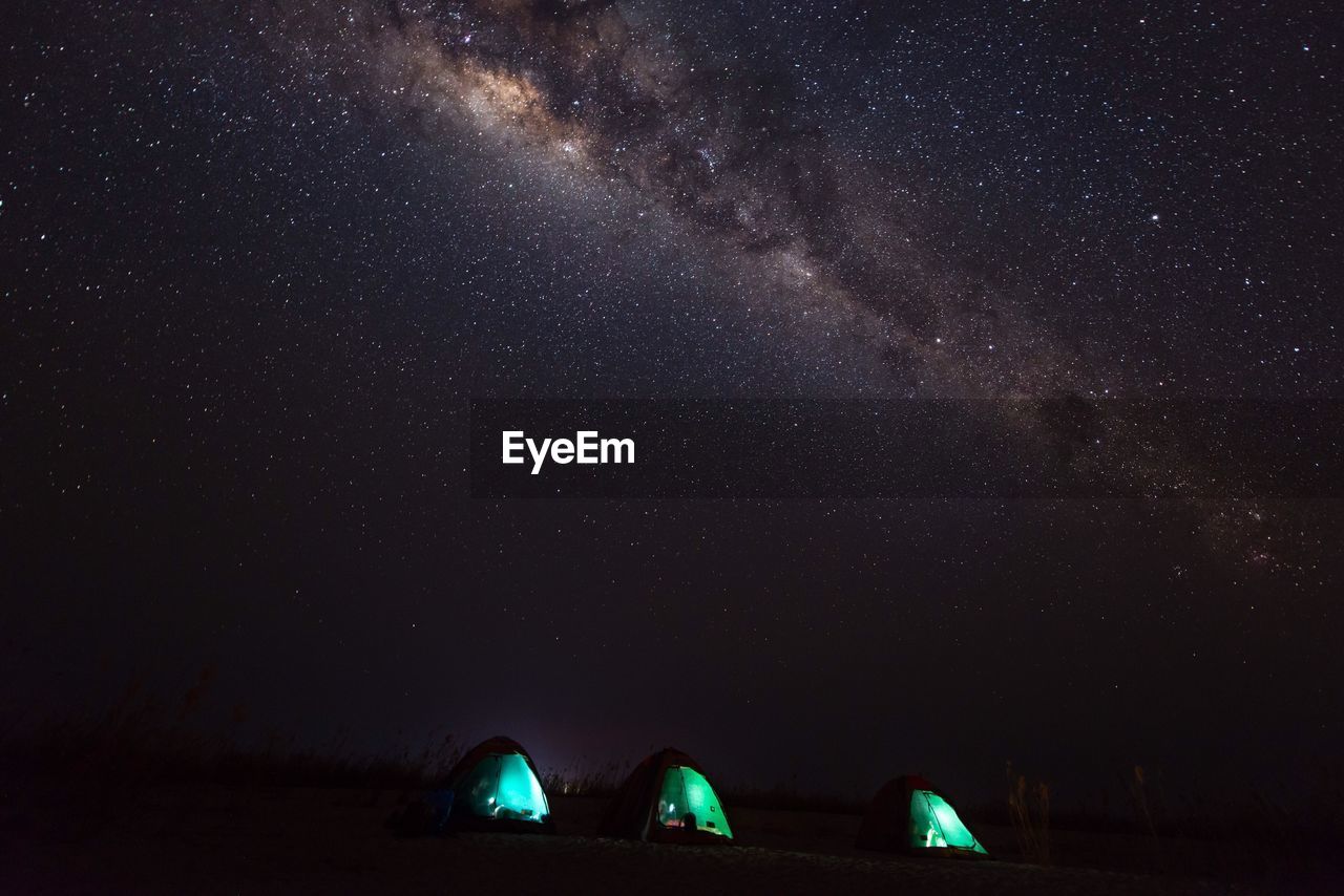 Illuminated tents on field against milky way at night