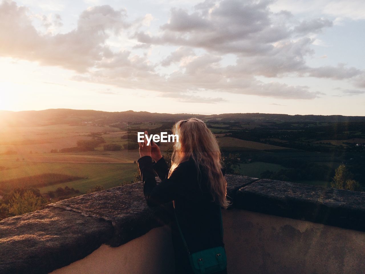 Woman photographing landscape through mobile phone during sunset