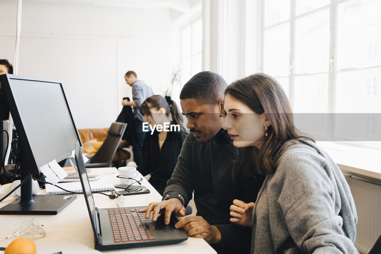 Focused software programmers coding on laptop while sitting in office