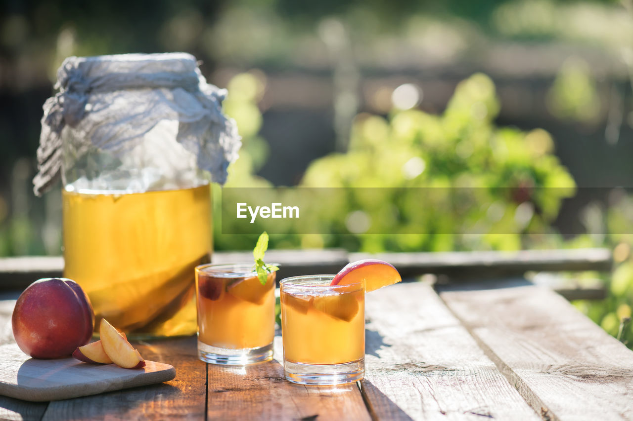 food and drink, food, drink, refreshment, wood, healthy eating, fruit, freshness, summer, table, drinking glass, wellbeing, glass, nature, household equipment, no people, container, sunlight, focus on foreground, outdoors, day, yellow, produce, alcoholic beverage, juice, citrus fruit, alcohol, jar