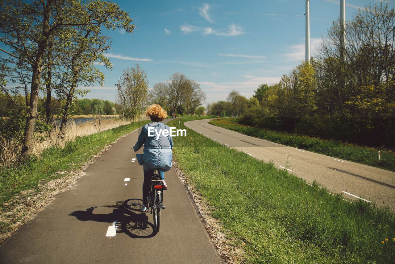 Rear view of woman with curly hair riding bicycle on road