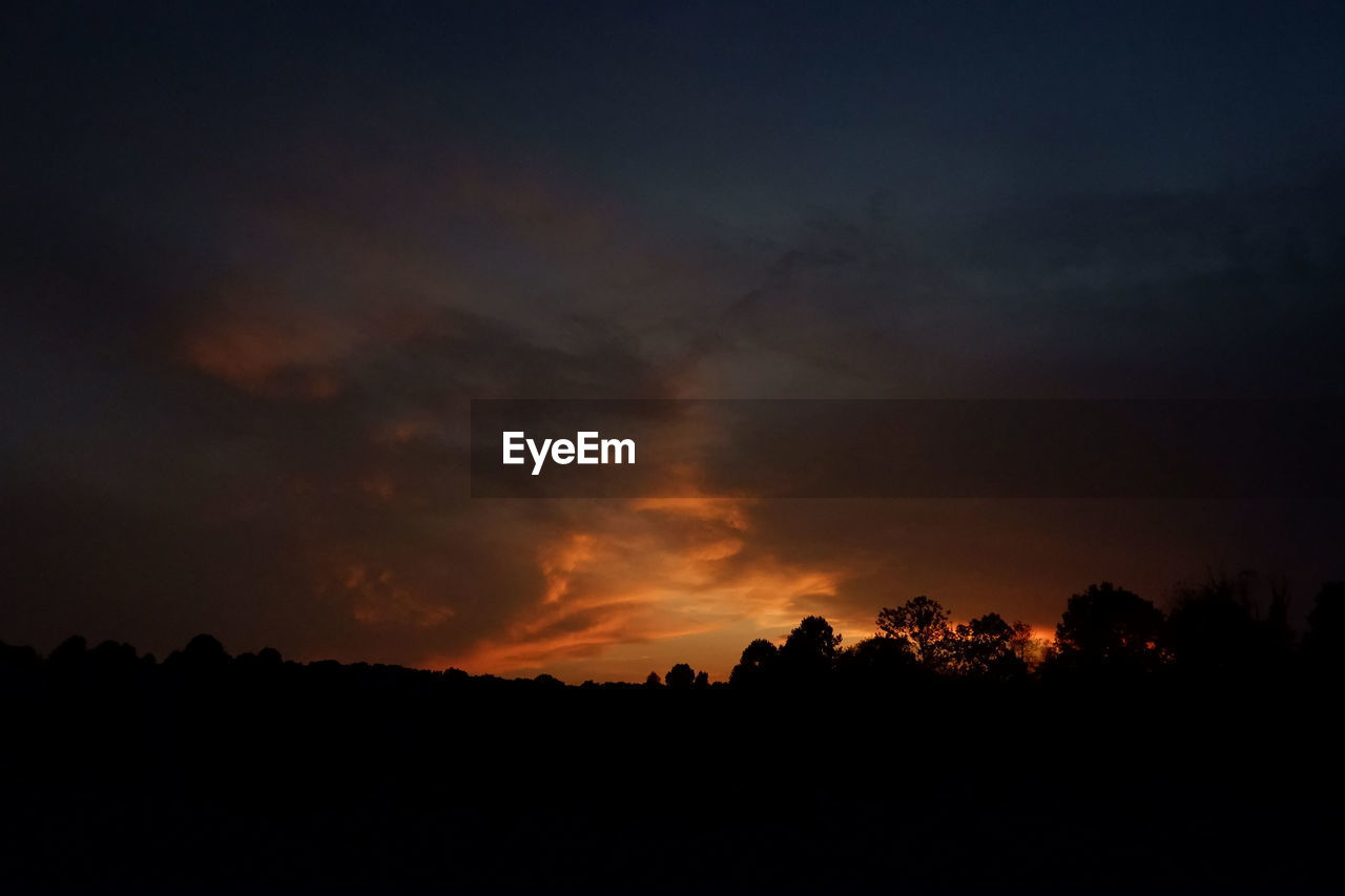 Silhouette trees against dramatic sky during sunset