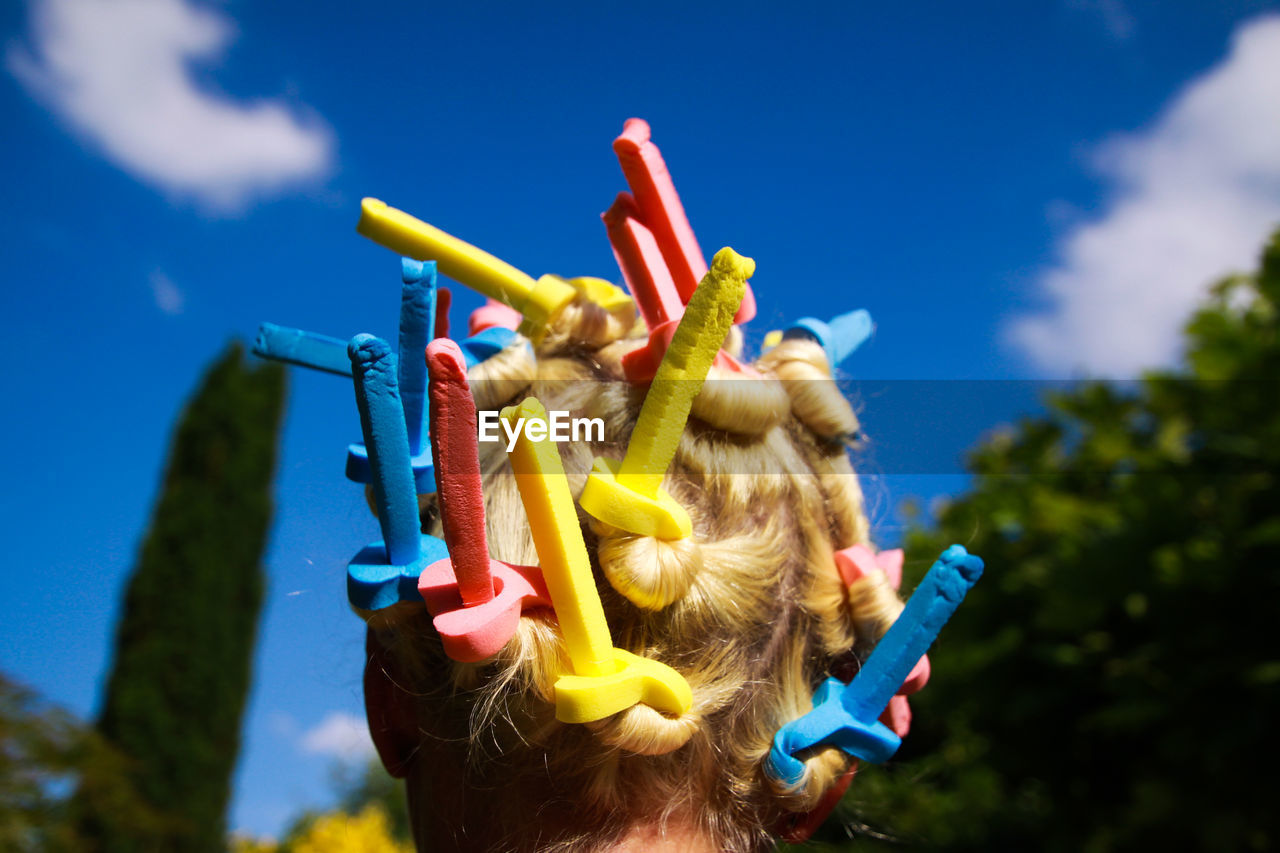 Woman wearing hair curlers against blue sky