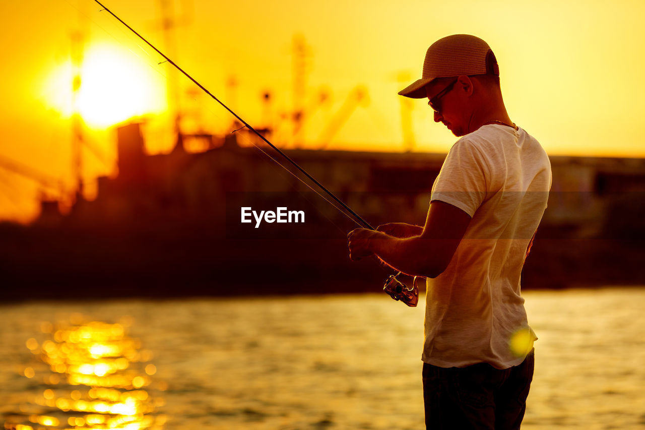sunset, water, one person, men, sky, nature, sea, fishing, adult, activity, rod, dusk, hat, fisherman, fishing rod, angling, standing, three quarter length, sun, evening, casting, holding, person, lifestyles, summer, motion, nautical vessel, silhouette, sports, beach, yellow, outdoors, leisure activity, beauty in nature, occupation, clothing, sunlight, recreation, relaxation, fly fishing, back lit