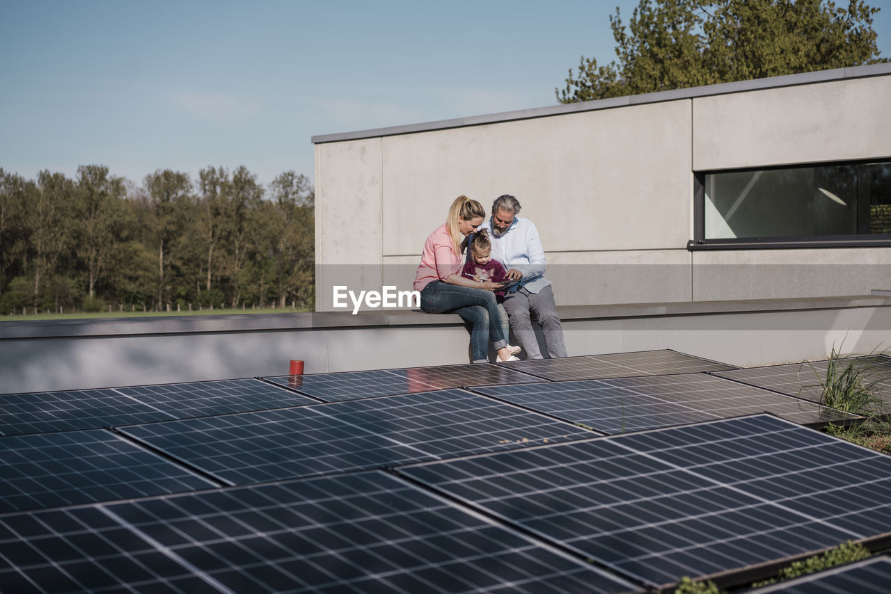 Man and woman with daughter sitting on wall by solar panel