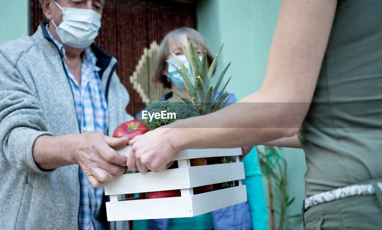 Midsection of woman giving crate to senior couple during pandemic
