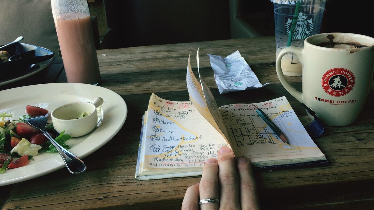 HIGH ANGLE VIEW OF HAND HOLDING BOOK ON TABLE AT HOME