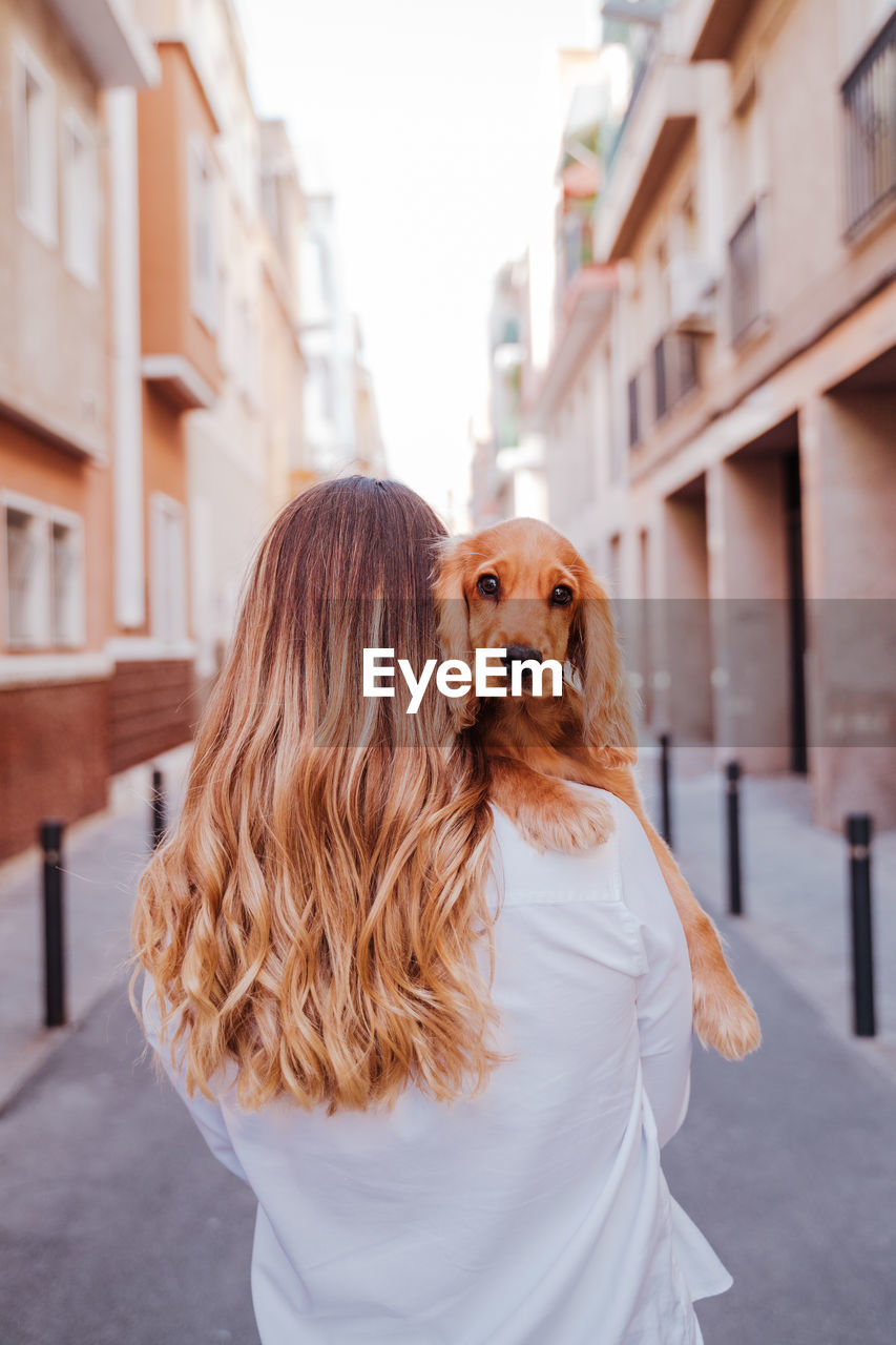 Woman carrying dog on street in city