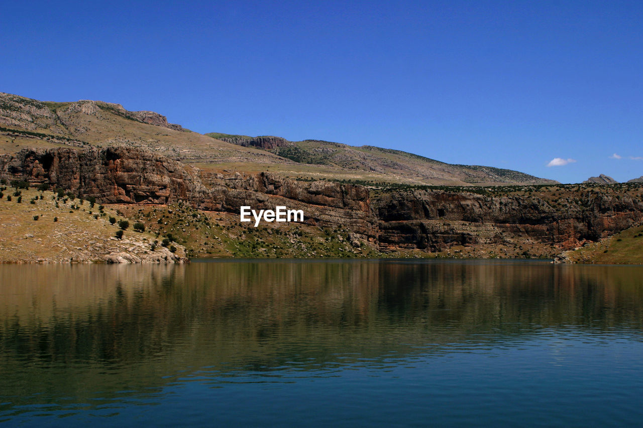 Scenic view of lake and mountains against clear blue sky