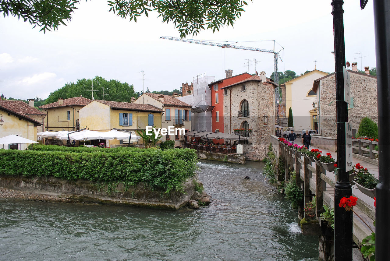 HOUSES BY RIVER AGAINST BUILDINGS IN CITY AGAINST SKY