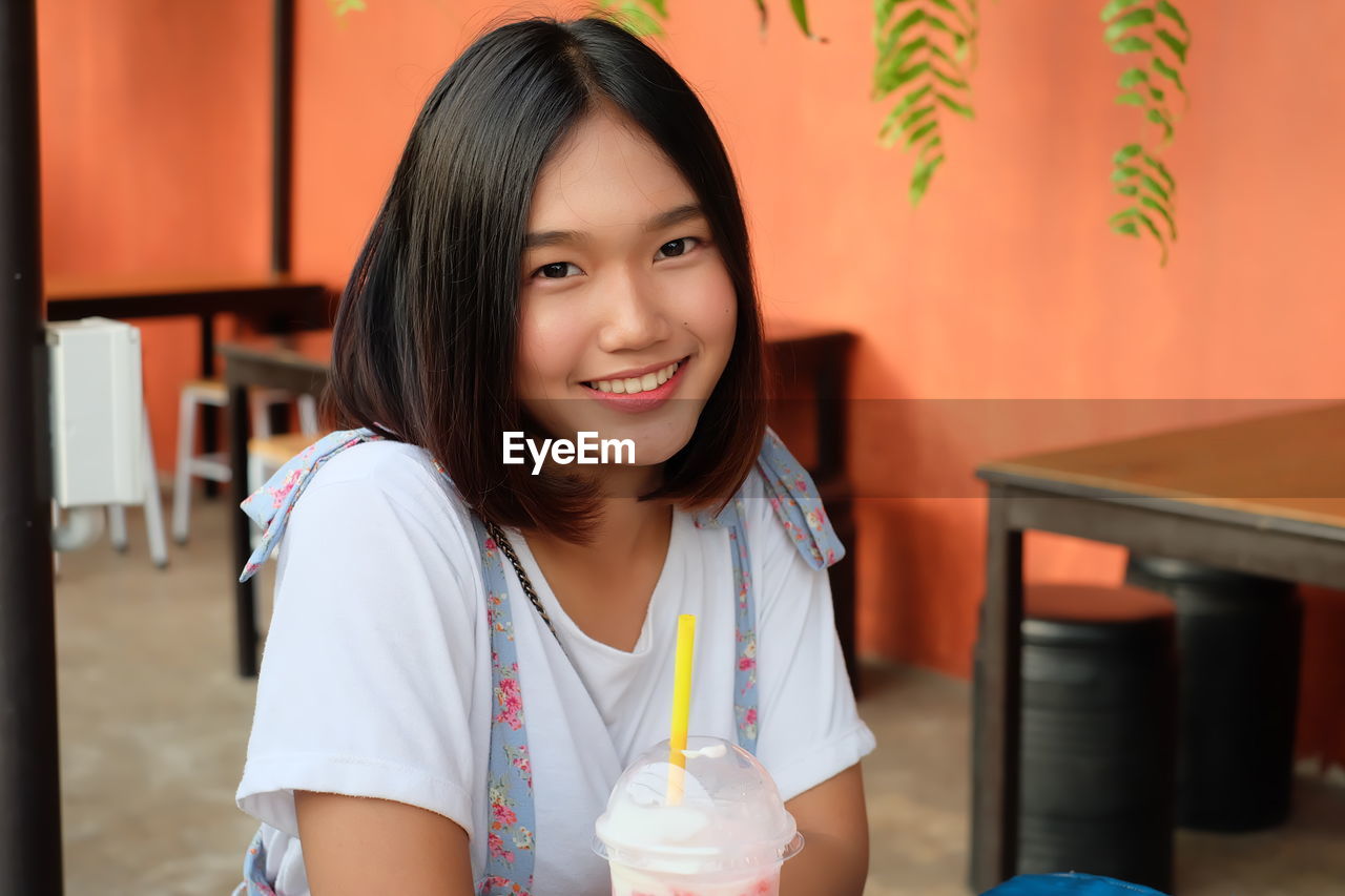 Portrait of smiling young woman sitting at sidewalk cafe