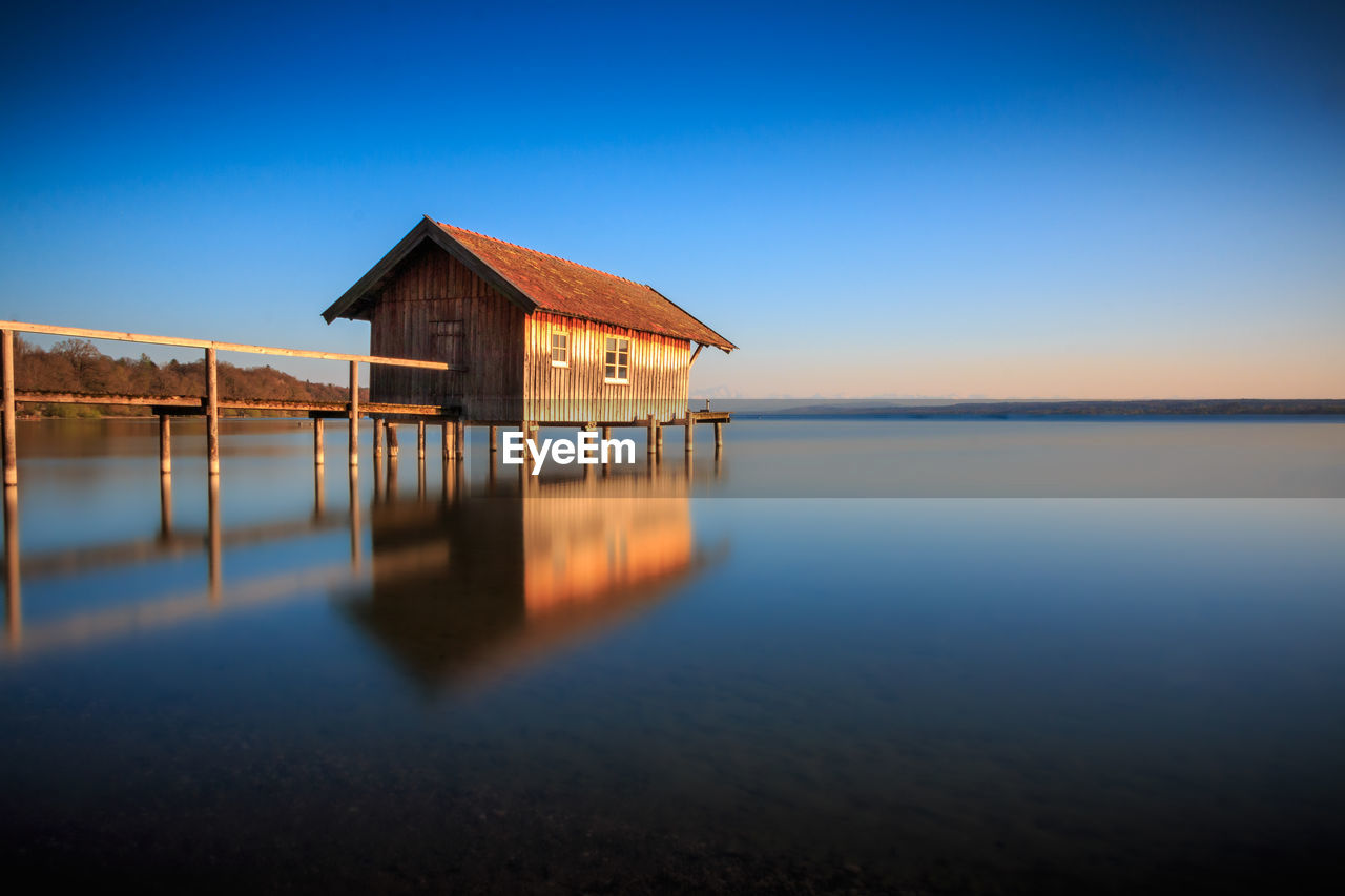 Stilt house in lake against clear sky during sunset