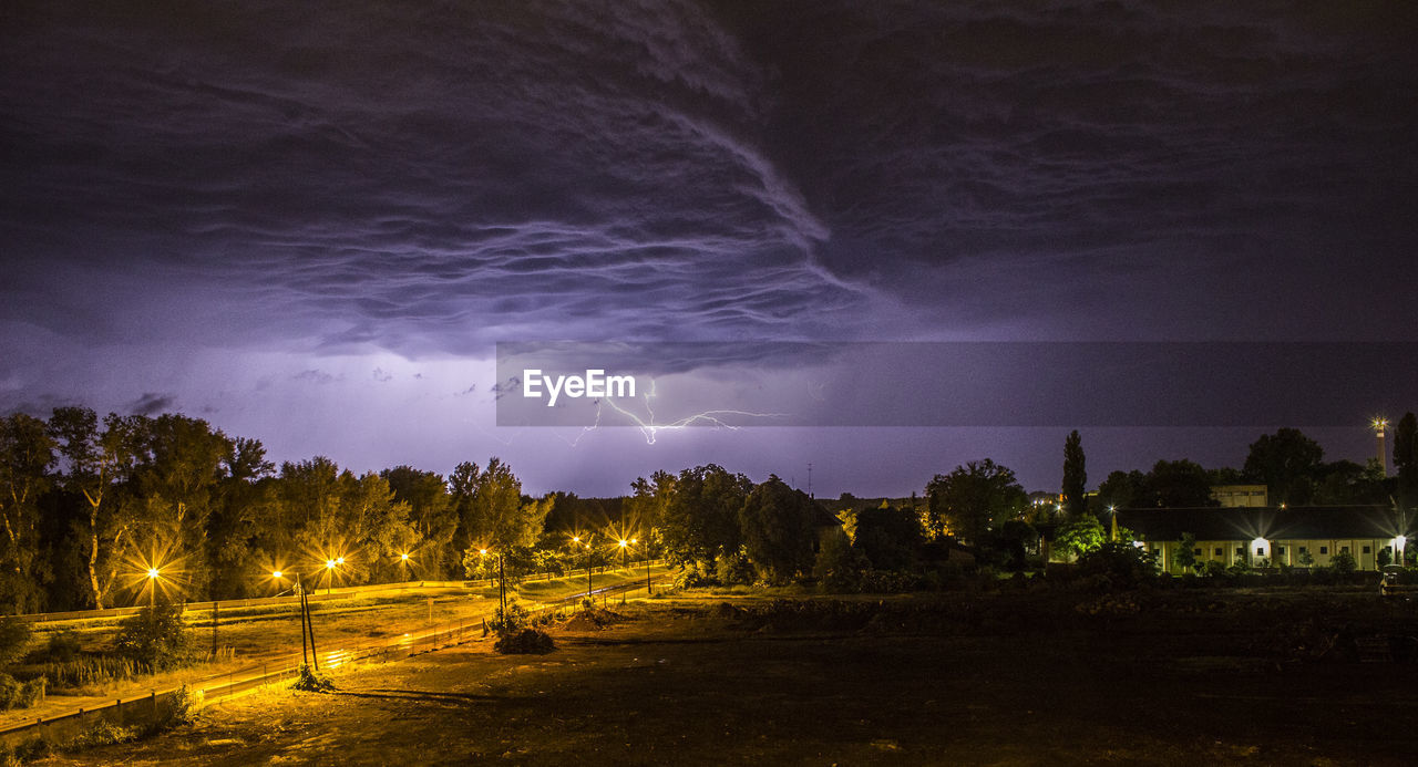 Low angle view of lightning over houses at dusk