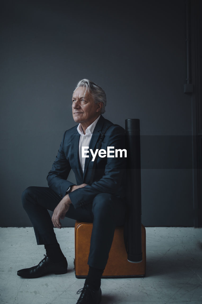 Senior businessman sitting on old-fashioned suitcase