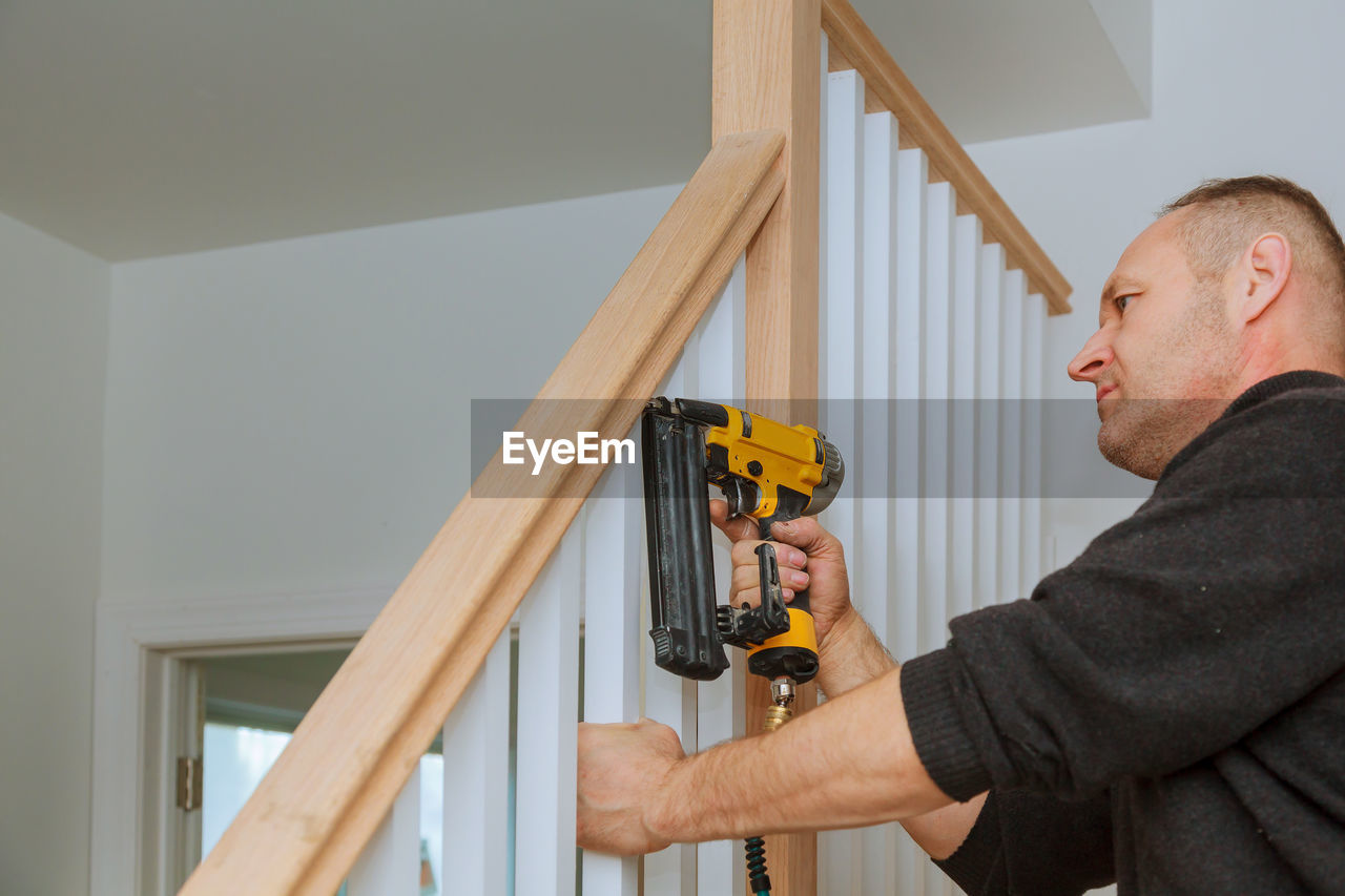 LOW ANGLE VIEW OF MAN WORKING ON WOODEN WALL AT HOME