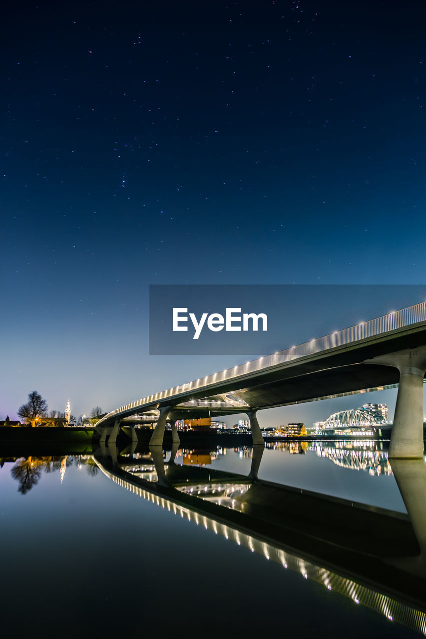 Low angle view of illuminated bridge over river against sky at night