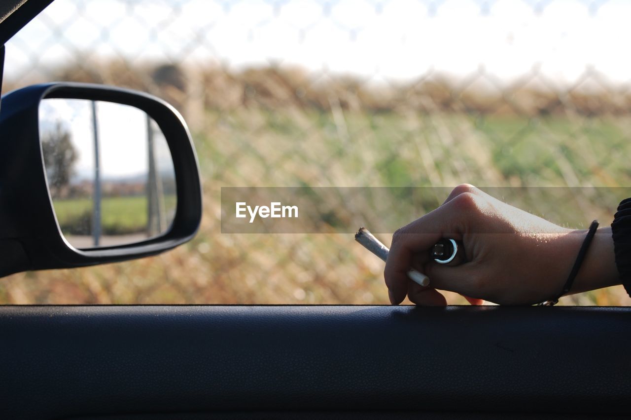 CLOSE-UP OF HAND HOLDING SIDE-VIEW MIRROR AGAINST SKY