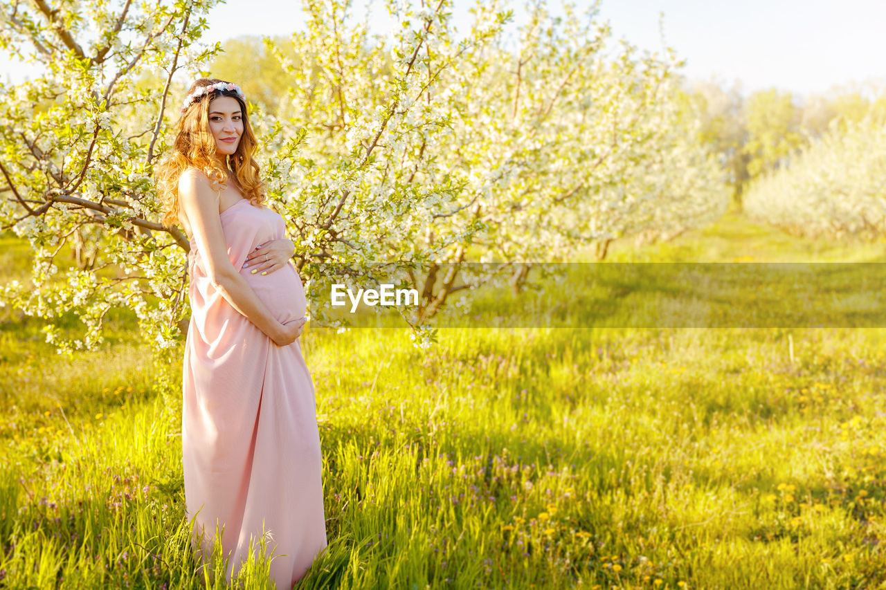 WOMAN STANDING ON FIELD BY TREE